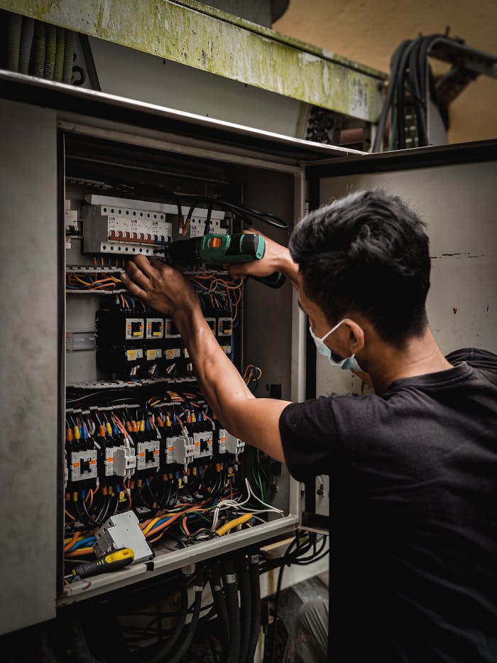 Technician working on circuit breaker panel, adjusting electrical wires indoors.